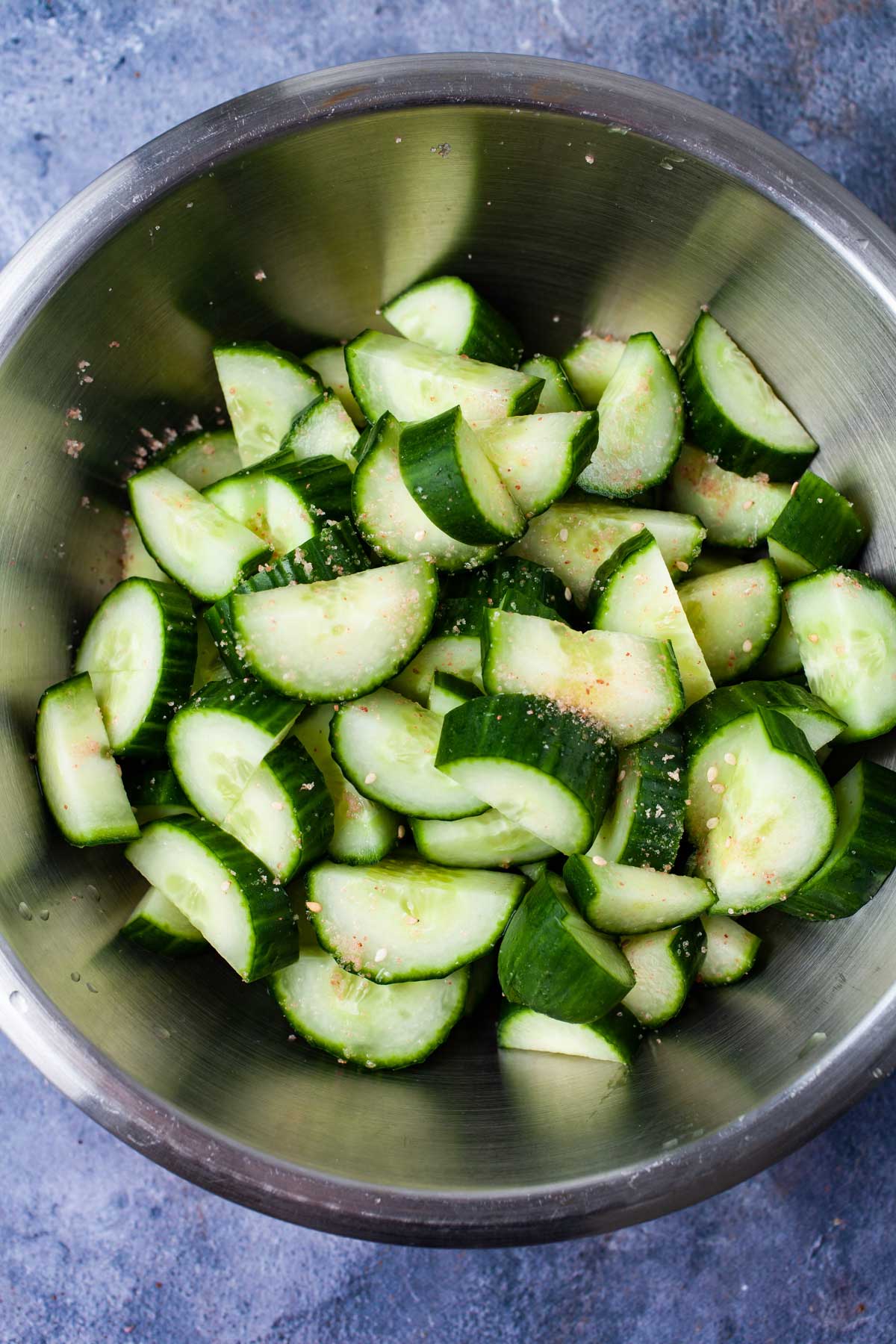 Salted chopped cucumbers in a stainless steel bowl.