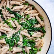 A garlic spinach pasta recipe with peas in a large Dutch pan topped with Parmesan Cheese.