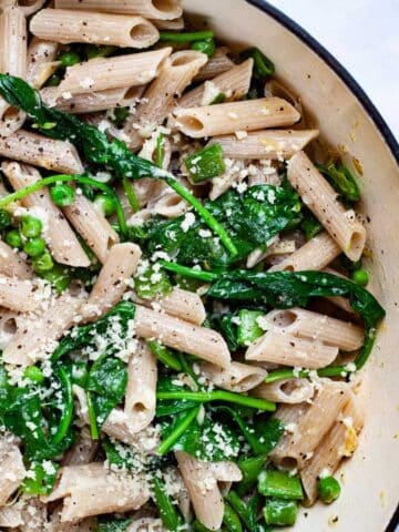 A garlic spinach pasta recipe with peas in a large Dutch pan topped with Parmesan Cheese.