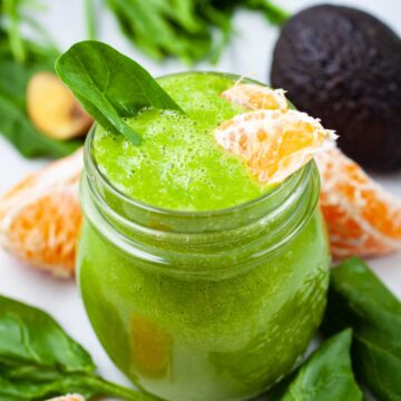 A creamy green orange smoothie Garnished with spinach leaves and fresh orange slices.