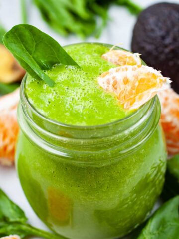 A creamy green orange smoothie Garnished with spinach leaves and fresh orange slices.