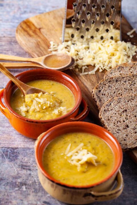 Two terra bowls filled with yellow squash soup and topped with Parmesan cheese.