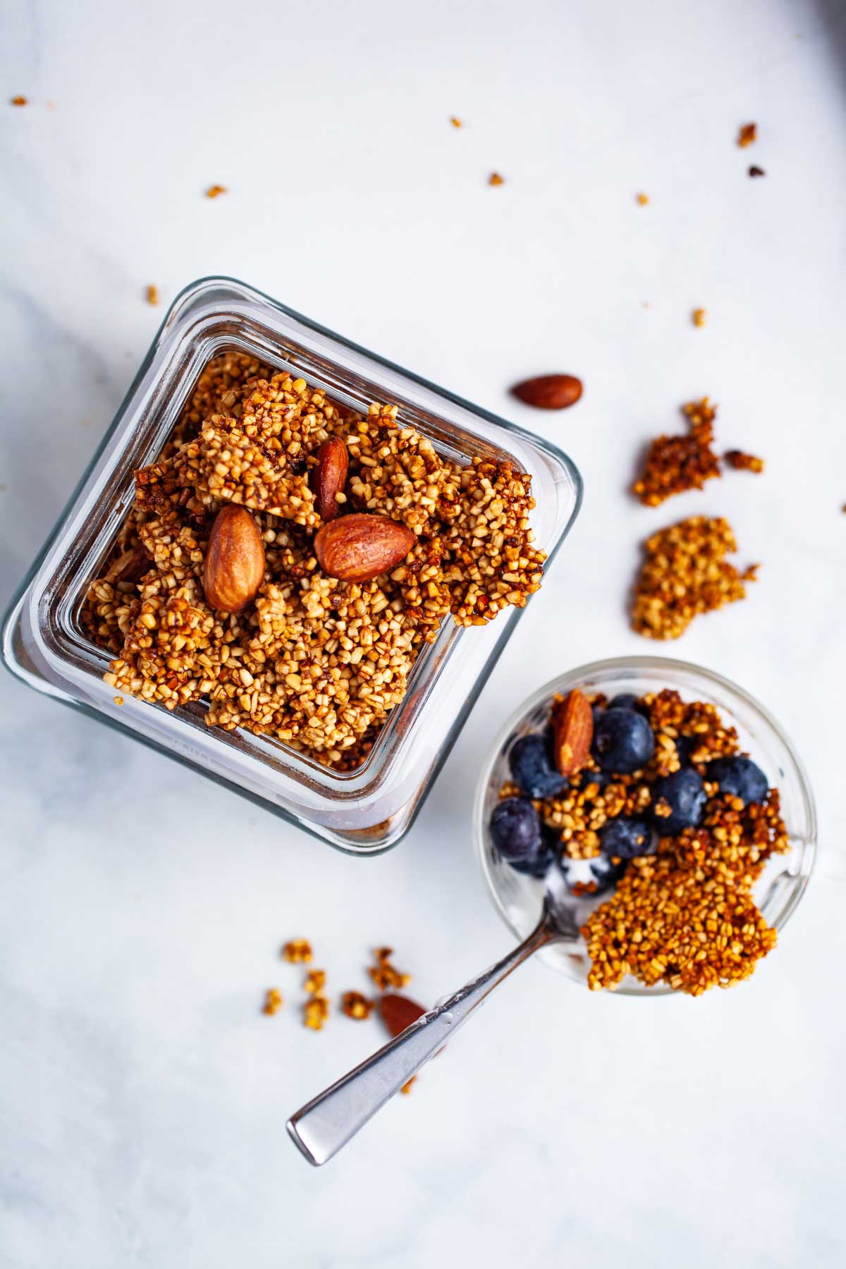 Golden brown clusters of steel-cut oats granola in a jar next to a small granola bowl with berries.