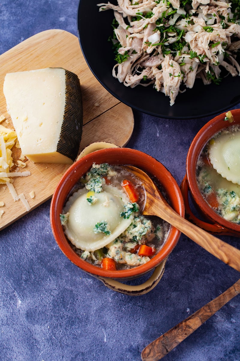 Two terra cotta bowls filled with vegetable pasta soup next to a board with parmesan cheese and a bowl with chicken salad on the side.