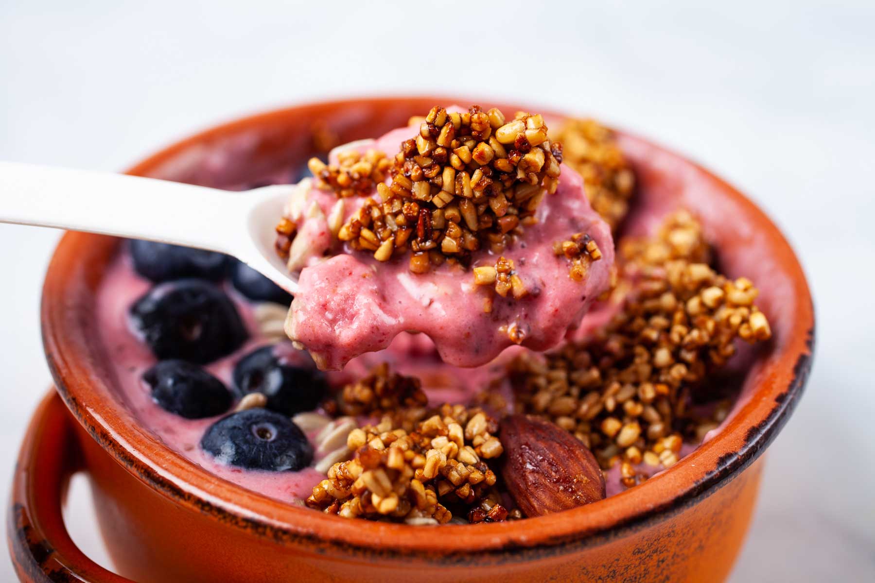 A hand holding a spoon with strawberry smoothie and toasted oats.