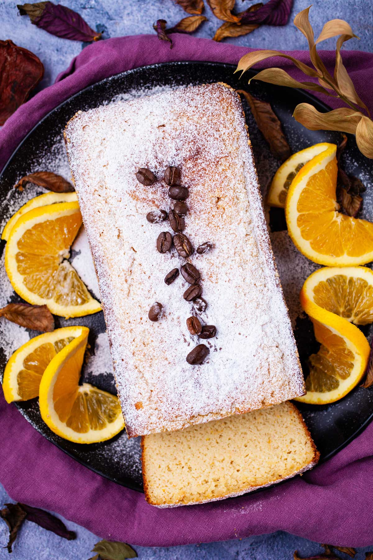 An almond flour coffee cake on a plate topped with sugar powder and garnished with coffee beans.