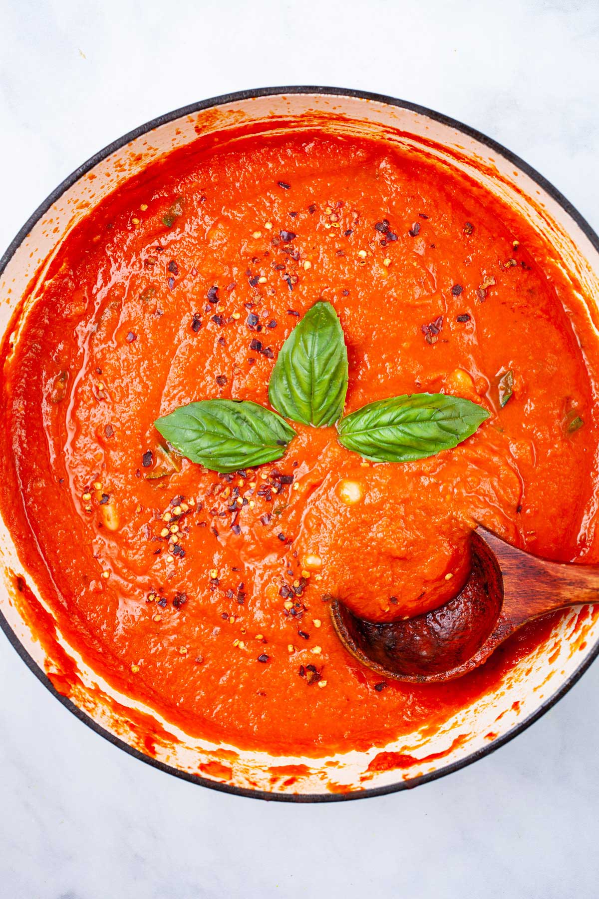 A sweet and spicy pasta sauce in a pan garnished with fresh basil leaves.