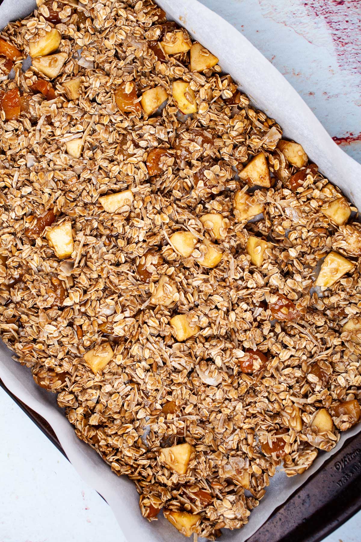 An oat mixture evenly spread over a large prepared baking pan, ready to go into the oven.