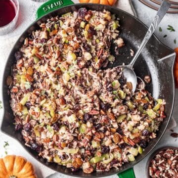 A spoon resting in a cast-iron pan with Thanksgiving rice dish.