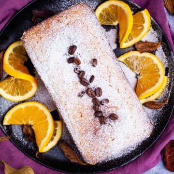 An almond flour coffee cake on a plate topped with sugar powder and garnished with coffee beans.