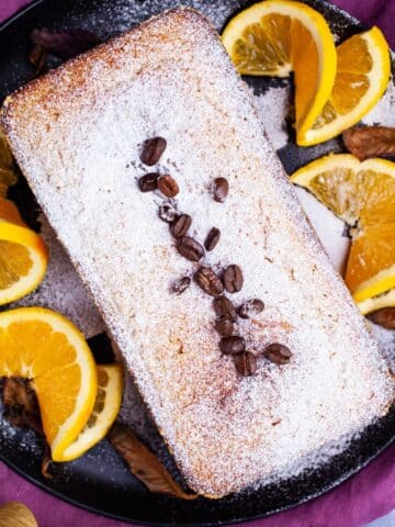 An almond flour coffee cake on a plate topped with sugar powder and garnished with coffee beans.