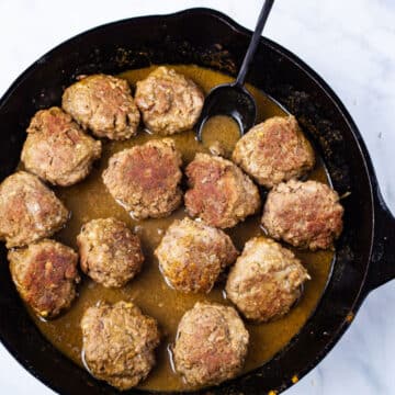 A spoon resting in a cast iron skillet with curried bison meatballs.