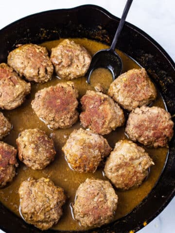 A spoon resting in a cast iron skillet with curried bison meatballs.