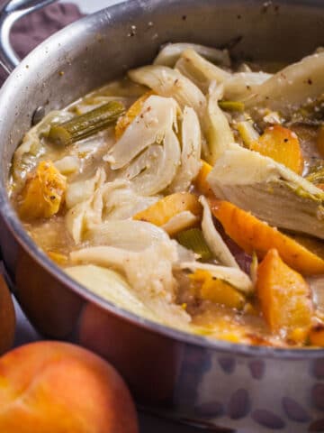 Soft braised fennel pieces and peaches in a creamy liquid in a large pan.