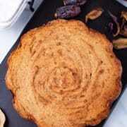 A brown baked date cake served on a wooden board.