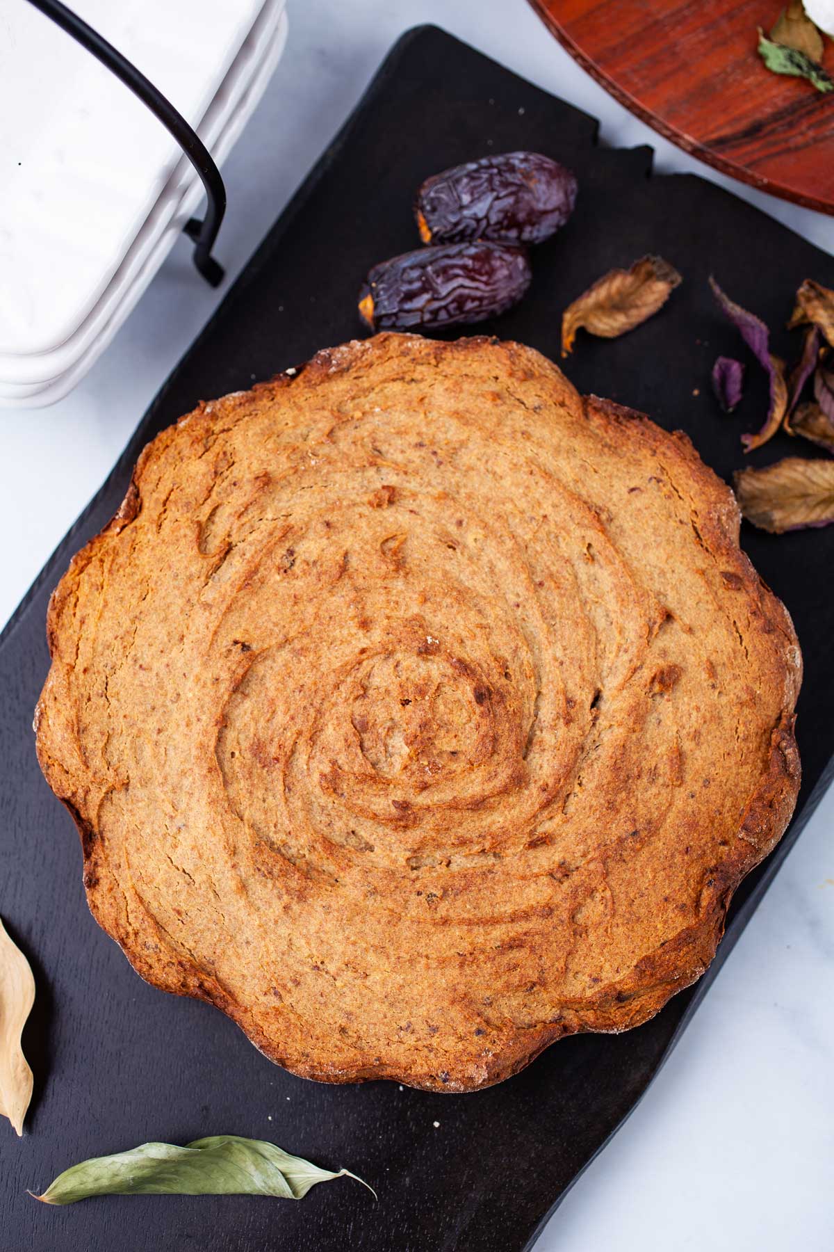 A brown baked date cake served on a wooden board.