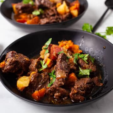 Two black plates filled with a hearty potato and beef stew.