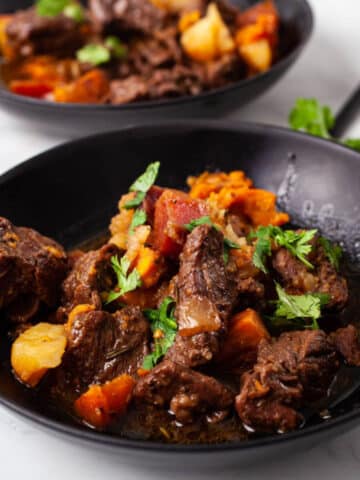 Two black plates filled with a hearty potato and beef stew.
