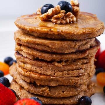 Oat flour pancakes stacked on top of each other and topped with maple syrup, nuts, and berries.