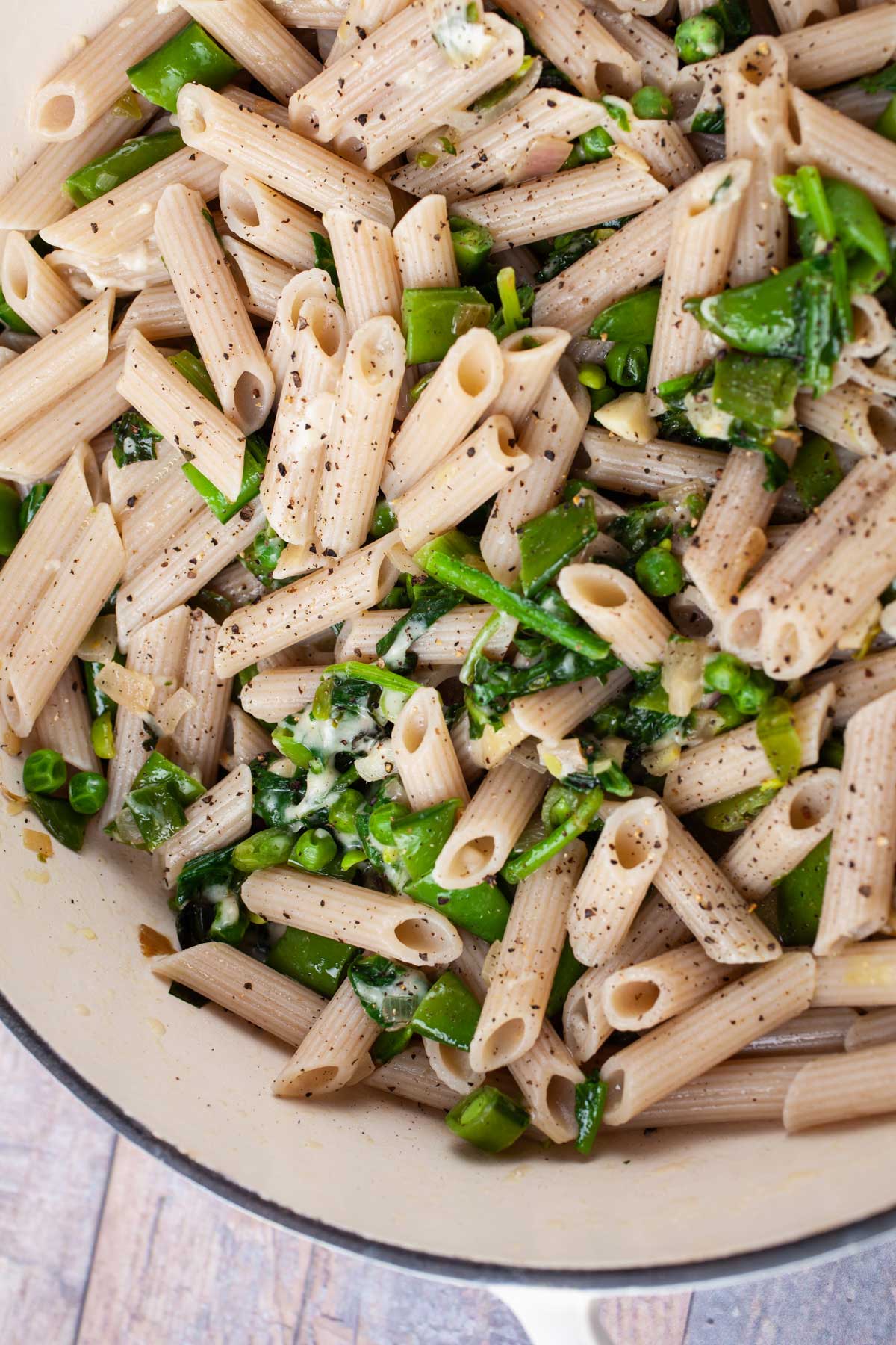 A garlic spinach pasta recipe with peas in a large Dutch pan topped with Parmesan Cheese.