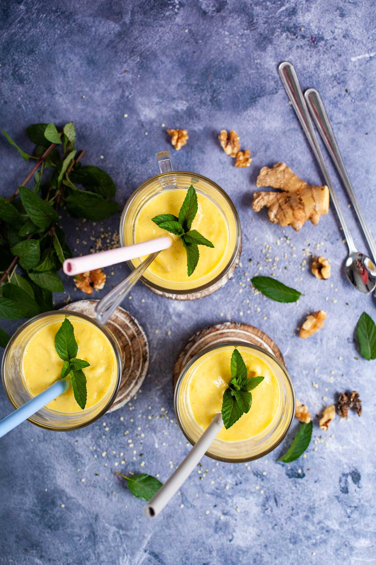 Three glasses filled with mango lassi, topped with mint leaves and each carrying a straw.