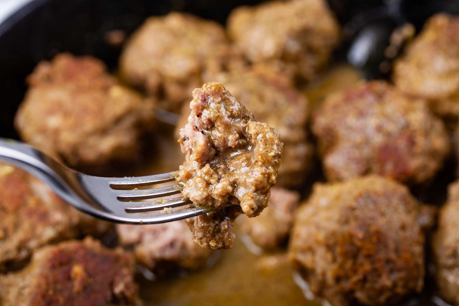 Someone holding up a fork with a piece of a tender bison meatball.