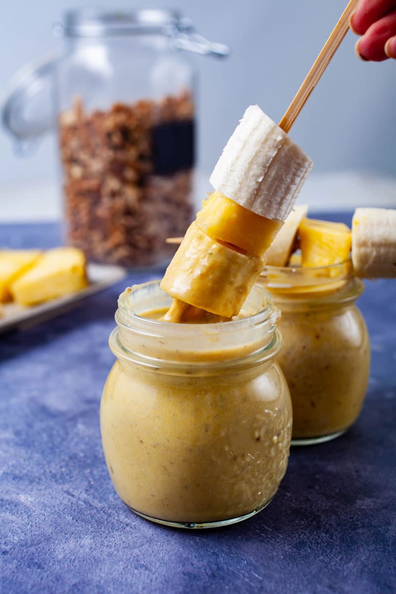 A hand dipping a fruit stick into a smoothie.