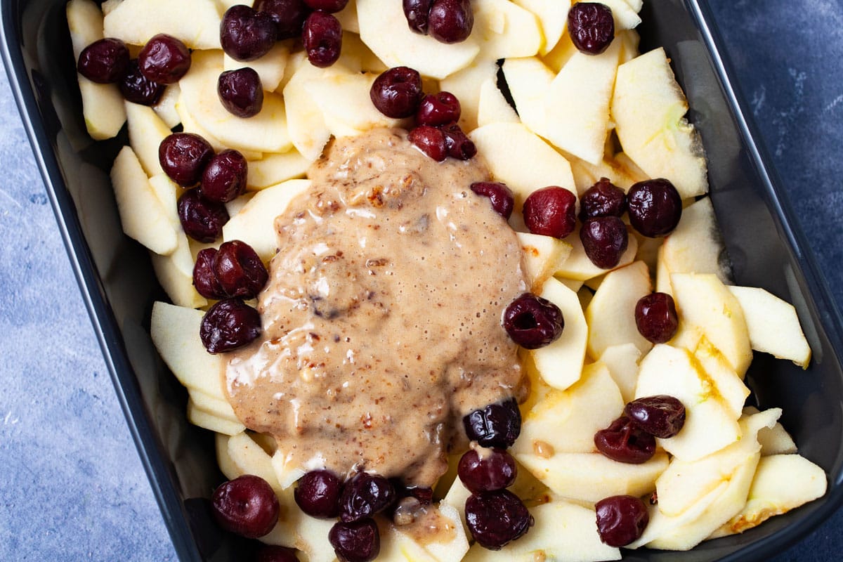 Sliced apples and cherries arranged in a baking pan and topped with a date paste.