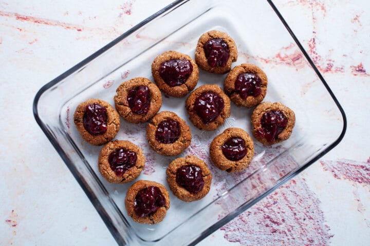 Thumbprint cookies stored next to each other in a glass container.