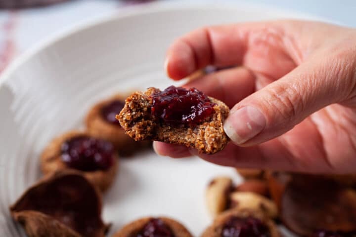 A hand holding a bitten Thumbprint cookie with jam.