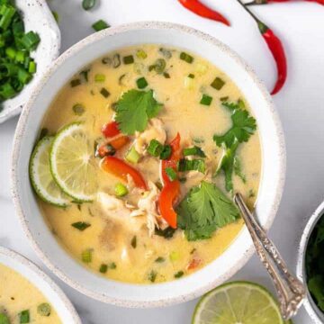 Tom ram ka soup topped with cilantro, lime and red belle pepper served in a small bowl.