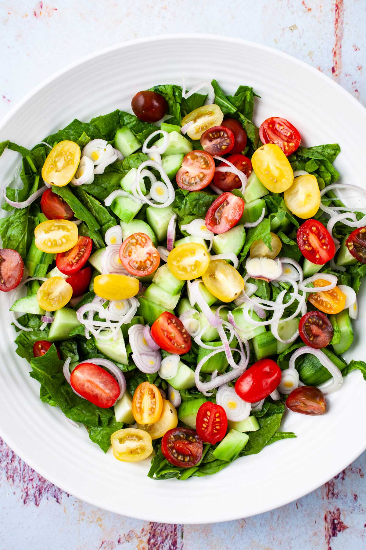 A large serving plate with a fresh medley of greens, cucumbers, onions, and cherry tomatoes.