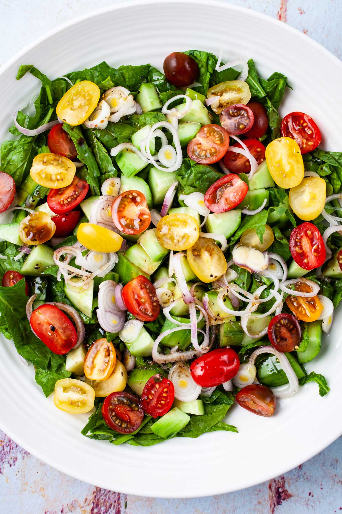 A large serving plate with a fresh medley of seasoned greens, cucumbers, onions, and cherry tomatoes.