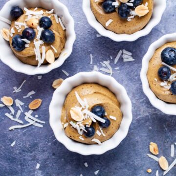 Small cups filled with vegan avocado mousse and topped with berries, peanuts, and coconut shreds.