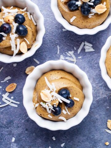 Small cups filled with vegan avocado mousse and topped with berries, peanuts, and coconut shreds.