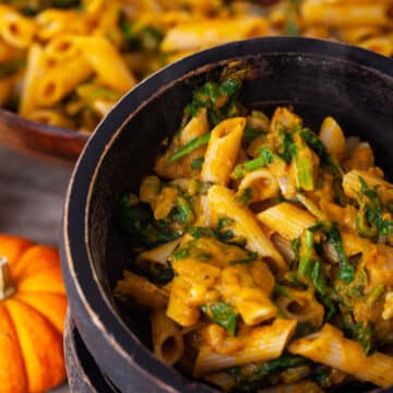 A close-up of two stacked wooden bowls with the bowl on top filled with a pumpkin spinach pasta.