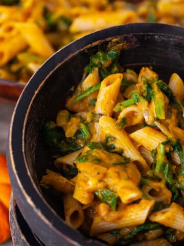 A close-up of two stacked wooden bowls with the bowl on top filled with a pumpkin spinach pasta.