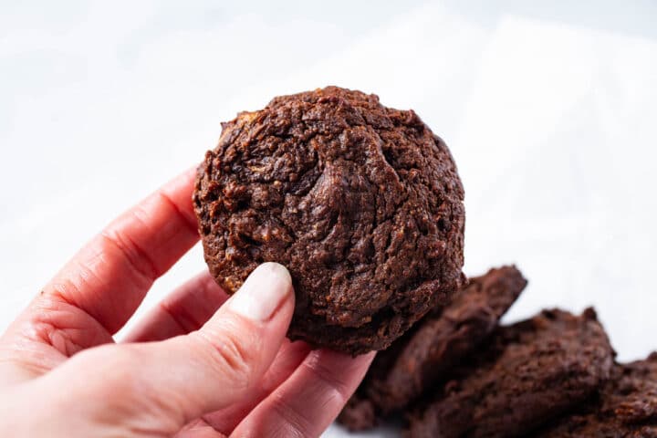 A hand holding up a soft baked cookie.