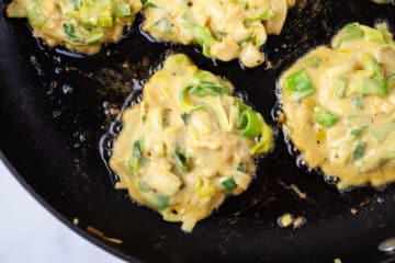 Batter of vegetable fritters sizzling in a pan.