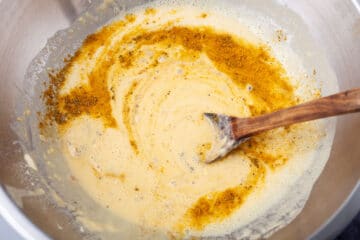 A spoon mixing seasoning in a batter.