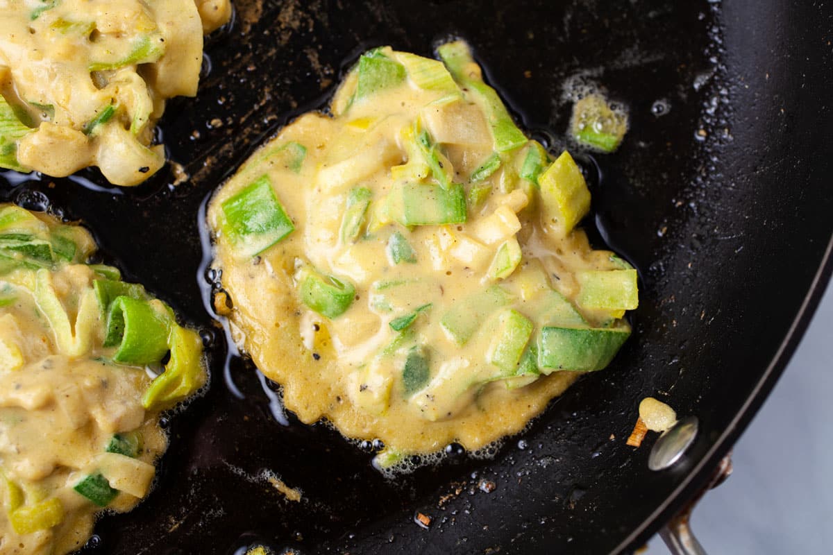 Batter of vegetable fritters sizzling in a pan.