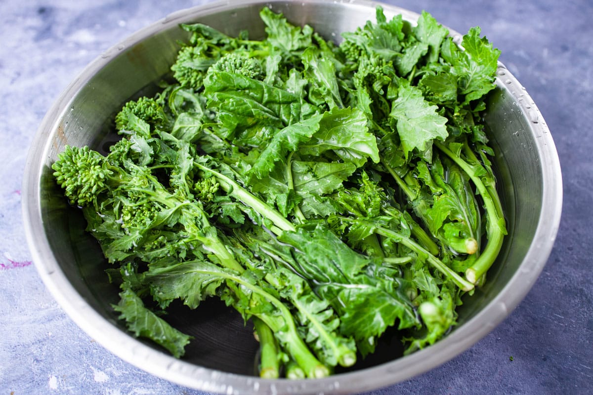 Broccoli rabe dunked in a stainless steel bowl with water.