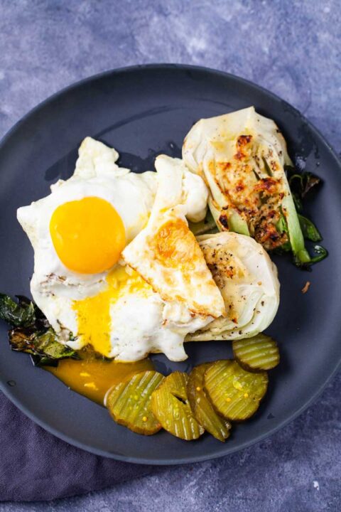 Two eggs sunny side up topped on roasted Chinese cabbage and served with pickles on the side.