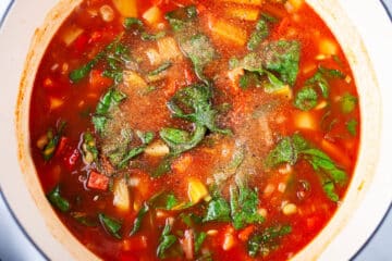 Seasoning added to a vegetable soup in a Dutch pan.