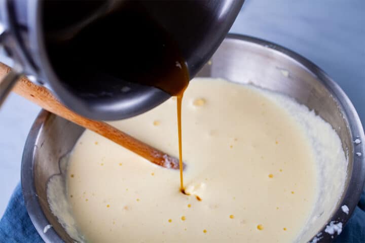 A brownish liquid drip coming from a saucepan into a mascarpone mixture in a bowl.