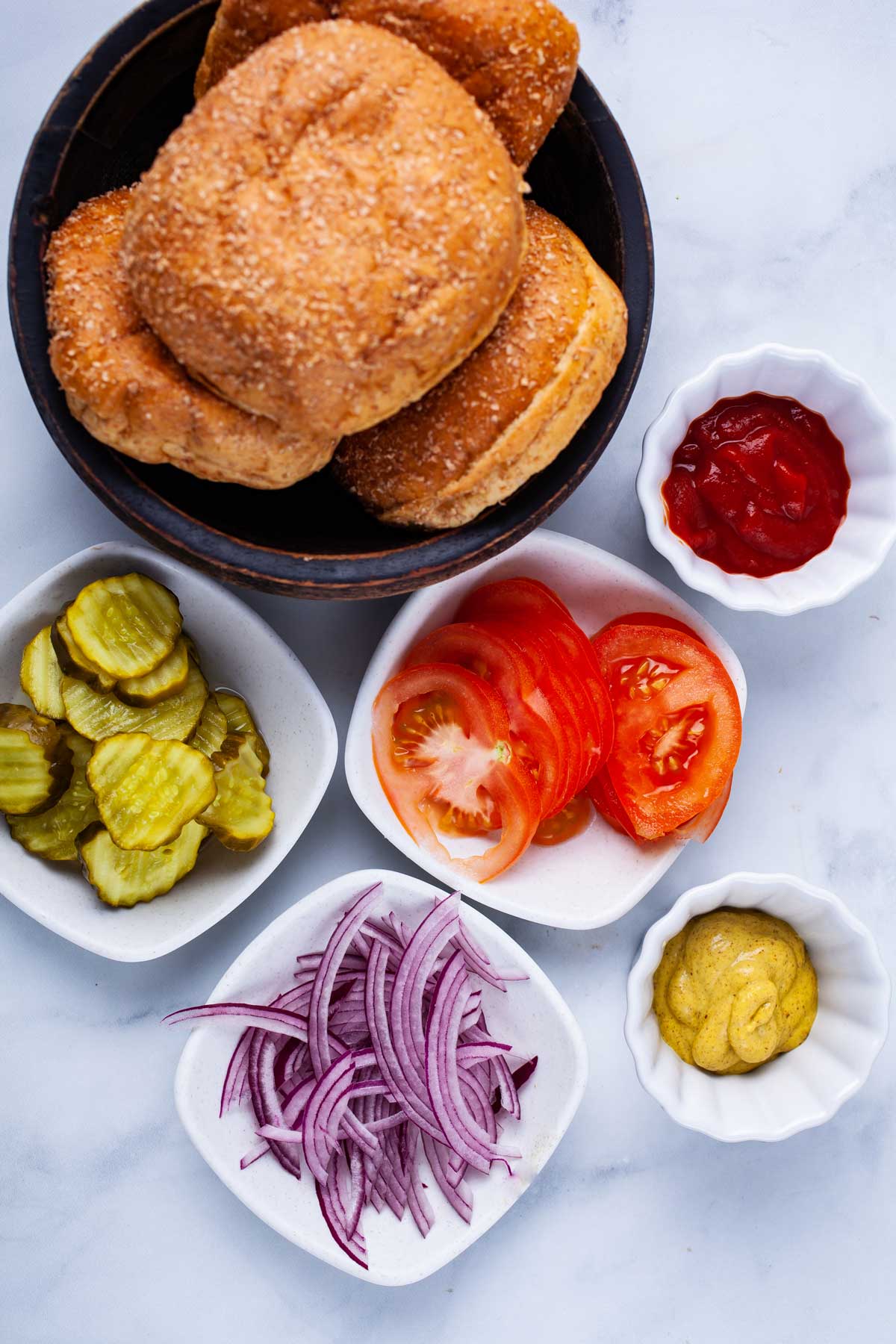 Condiments like ketchup, mustard, pickles, sliced red onions, tomato slices, and burger buns displayed on the table.