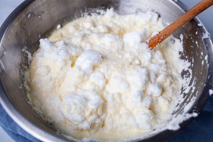 A spatula folding stiffed egg whites into wet ingredients in a stainless steel bowl.