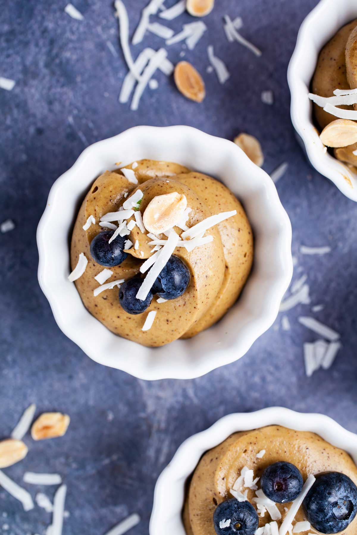 Small cups filled with vegan avocado mousse and topped with berries and coconut shreds.