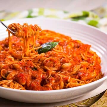 A fork lifting a bite out of a plate with spaghetti noodles drenched in a red tomato sauce with beans.
