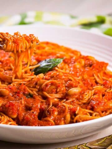 A fork lifting a bite out of a plate with spaghetti noodles drenched in a red tomato sauce with beans.